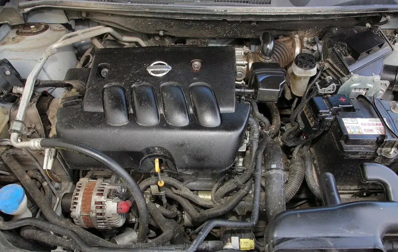 Silnik Nissan Qashqai J10, widok z góry. Czarna pokrywa silnika z logo Nissan, alternator, akumulator i przewody.