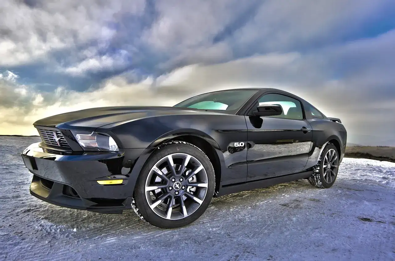 Czarny Ford Mustang GT 5.0, jeden z tych tanich sportowych aut, zaparkowany na zaśnieżonej drodze pod dramatycznym niebem.