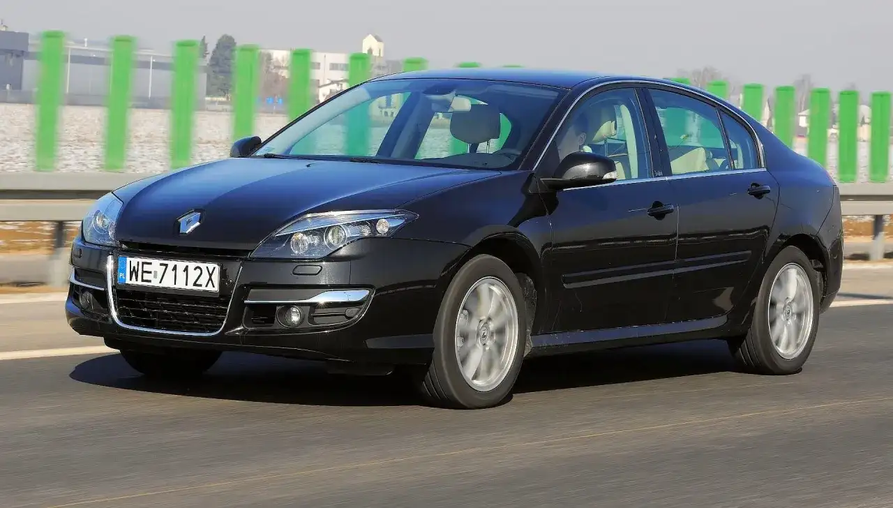 Czarny Renault Laguna 3 2.0 dCi jedzie po drodze, za zielonymi słupkami.