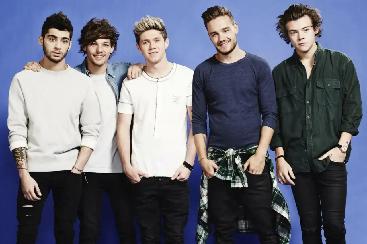 Pięciu członków One Direction pozuje do zdjęcia na niebieskim tle.