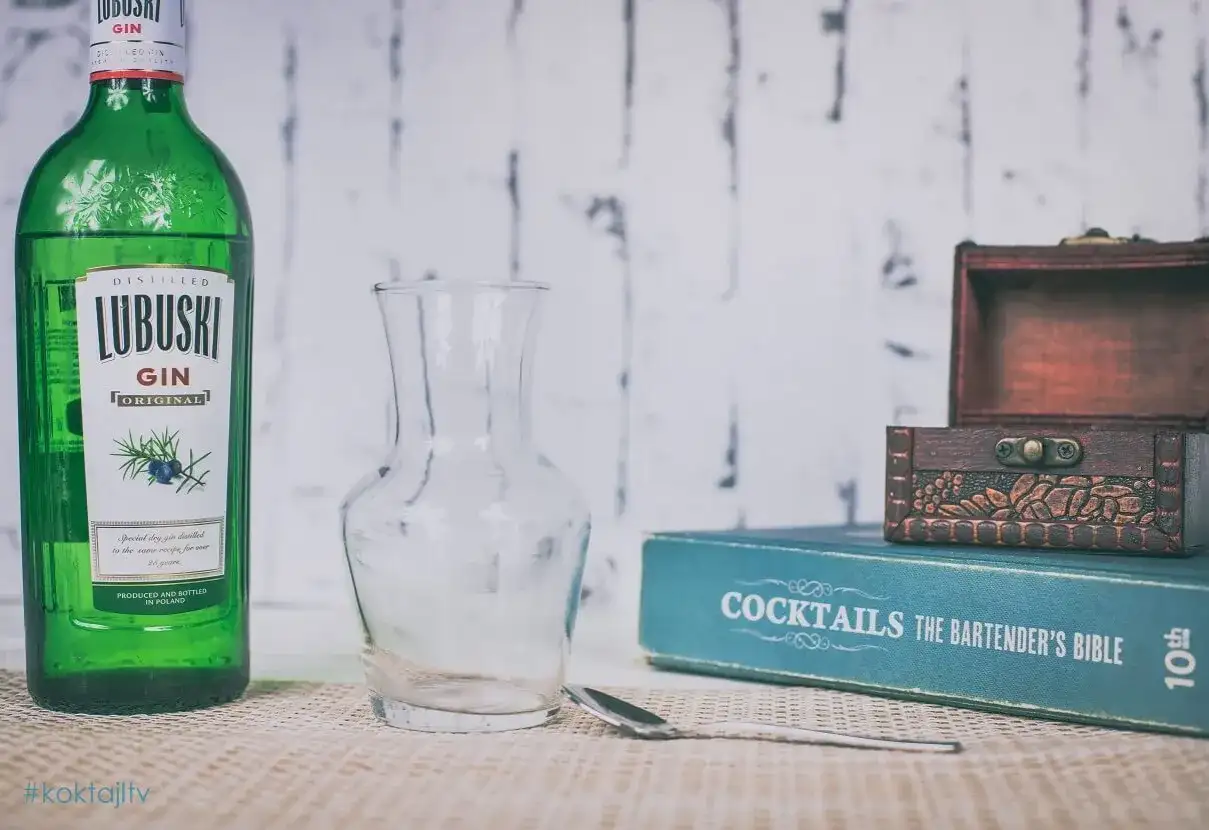 Butelka Lubuski Gin, pusta karafka, łyżka barmańska i książka "Cocktails The Bartender's Bible" sugerują przygotowanie drinków.