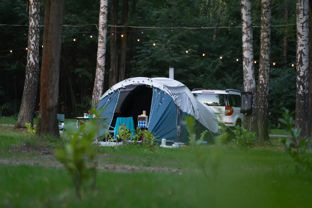 Namiot i samochód w lesie, idealne miejsce na ferie 2026 śląskie. Girlanda świetlna dodaje uroku.