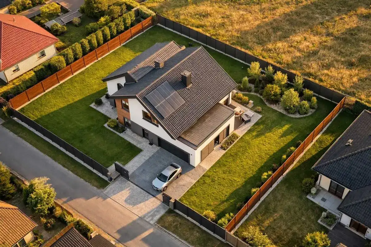 Nowoczesny dom z panelami słonecznymi i zadbanym ogrodem. Obiekt małej architektury, jak altana, jest widoczny w oddali. Odległość od granicy działki jest zachowana.