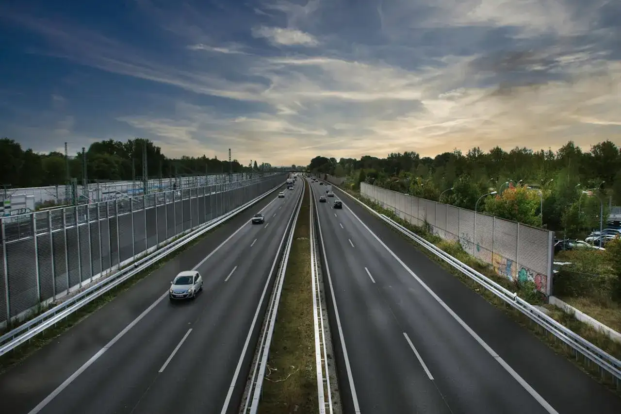 Szeroka autostrada A2 z ruchem samochodowym, otoczona zielenią i ekranami akustycznymi.