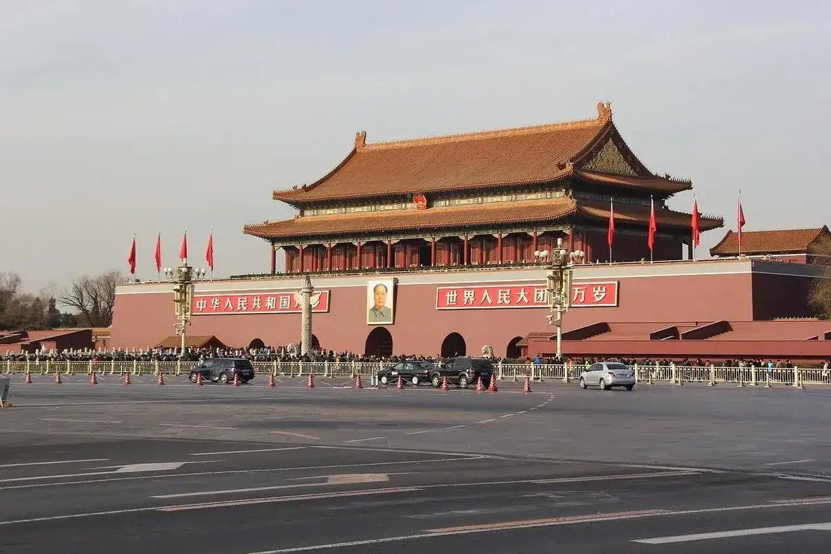 Brama **Tiananmen** w Pekinie, z portretem Mao i chińskimi napisami. Tłumy ludzi i samochody na placu.