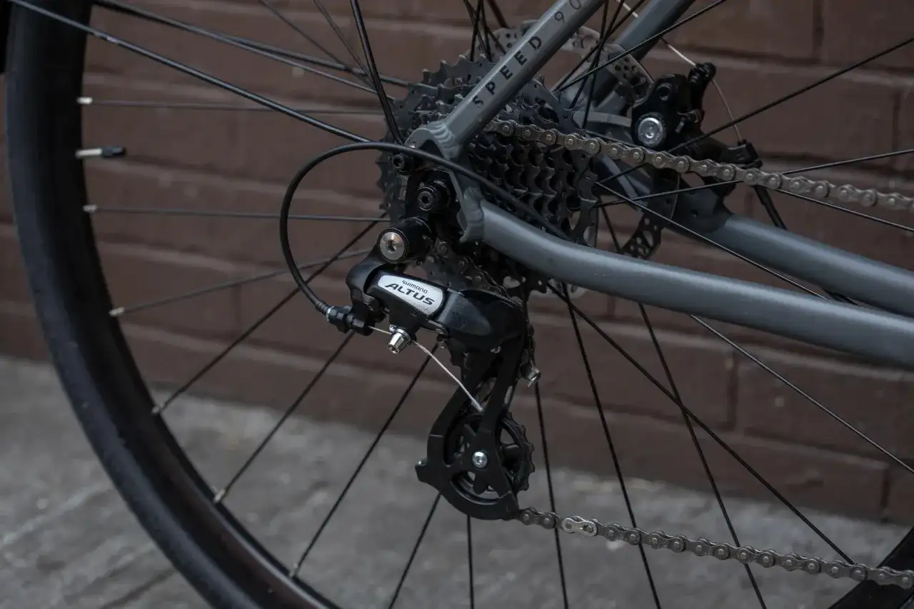 Tylna przerzutka Shimano Altus z widocznym hakiem do przerzutki, kasetą i łańcuchem na rowerze.