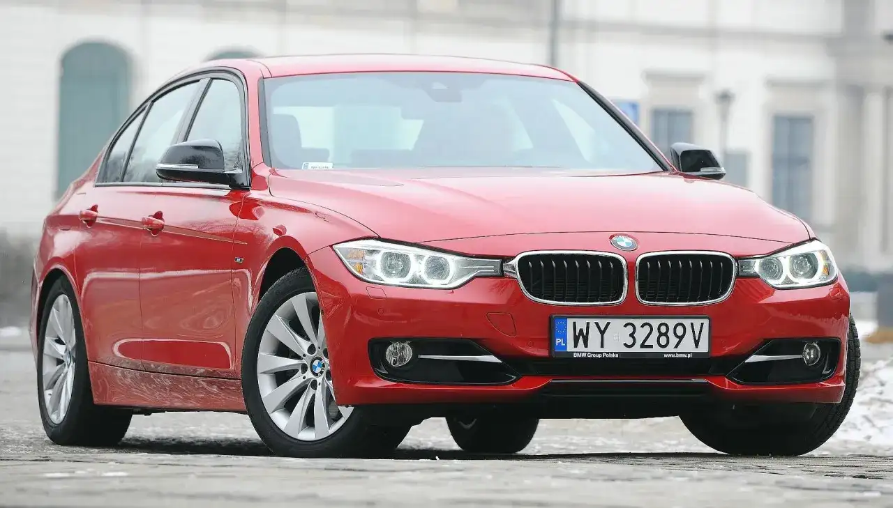 Czerwone BMW 3 F30 z polskimi tablicami rejestracyjnymi WY 3289V zaparkowane na zewnątrz.