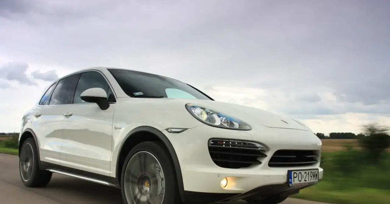 Biały Porsche Cayenne Turbo pędzi po drodze, chmury na niebie sugerują zmienną pogodę.