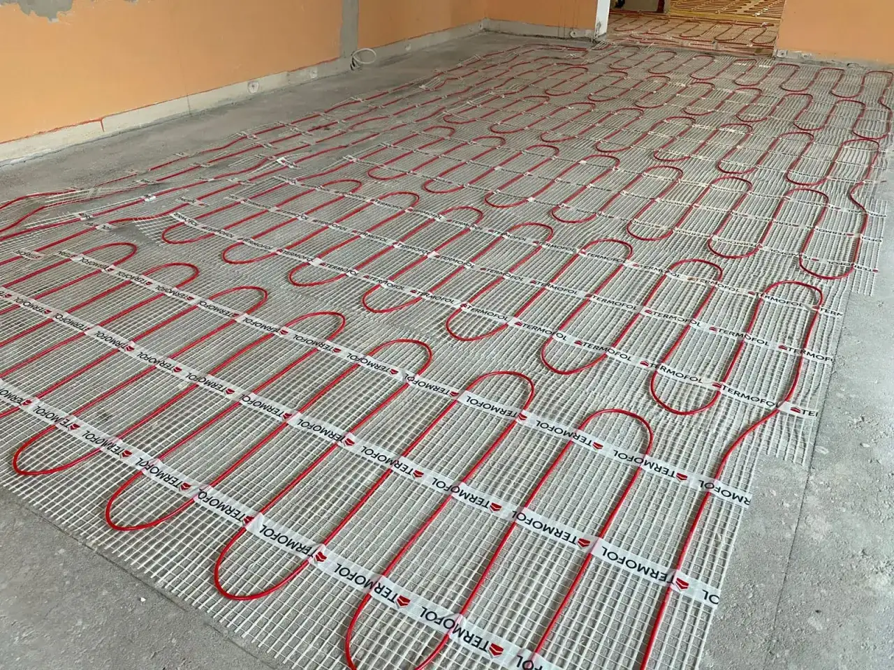 Instalacja ogrzewania podłogowego z czerwonymi rurkami na siatce, gotowa pod minimalna grubość wylewki betonowej.