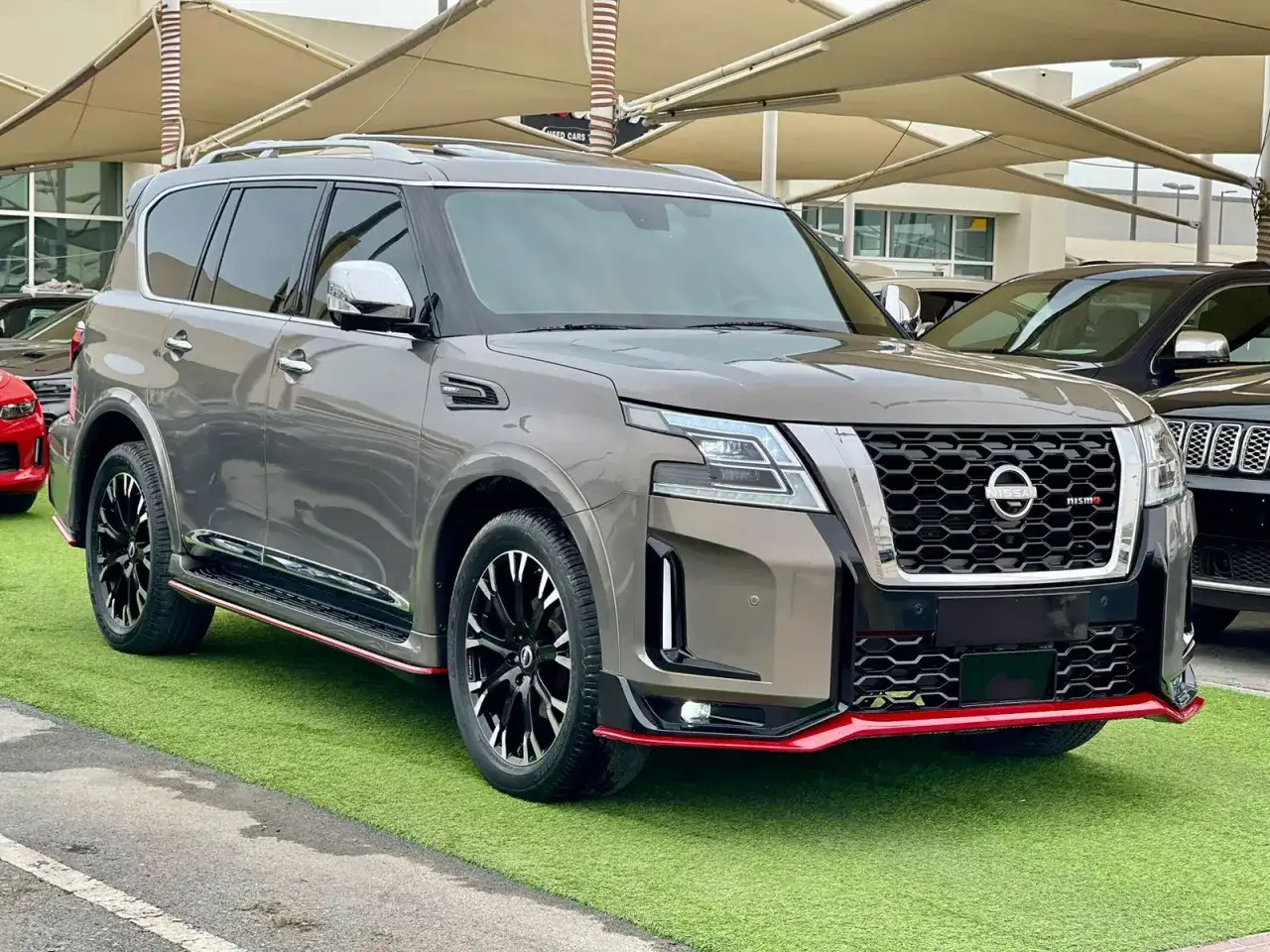 Szary Nissan Patrol 2025 Nismo z czerwonymi akcentami, prezentujący się na zielonej trawie.