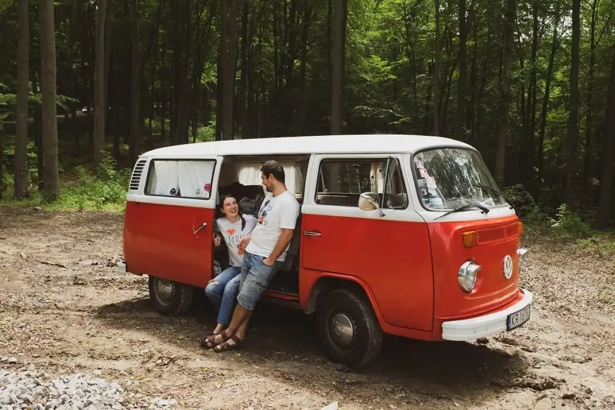 Para zakochanych odpoczywa przy swoim czerwono-białym vw t2 w lesie.