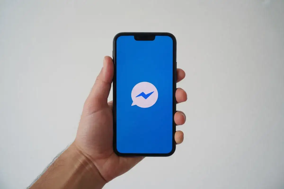 Dłoń trzyma smartfon z niebieskim ekranem i ikoną Messengera. Zastanawiasz się, dlaczego nie widzę aktywności na Messengerze?