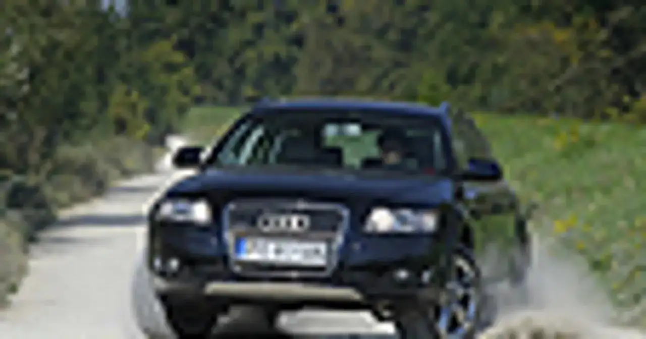 Ciemny Audi allroad pokonuje piaszczystą drogę, wzbijając kurz.