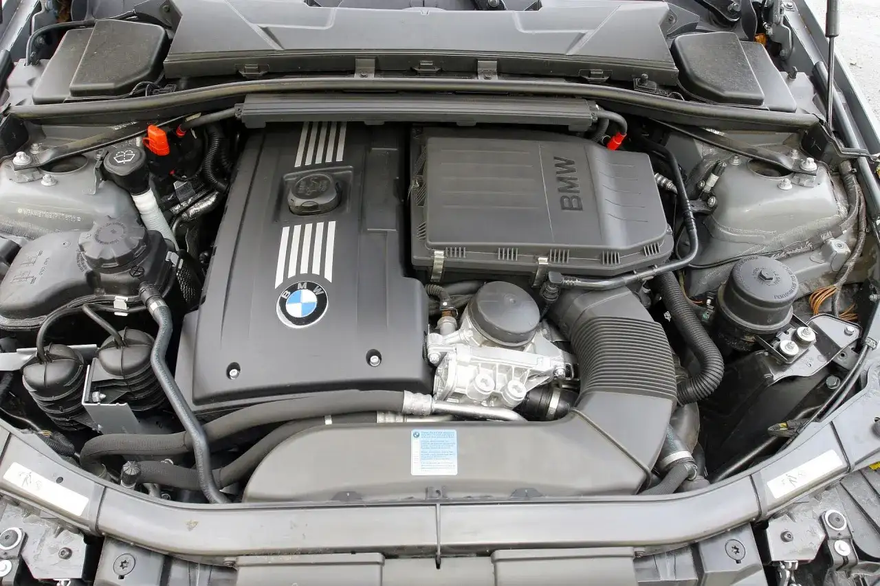 Silnik BMW 325i. Widok na pokrywę silnika z logo BMW, elementy układu dolotowego i chłodzenia.
