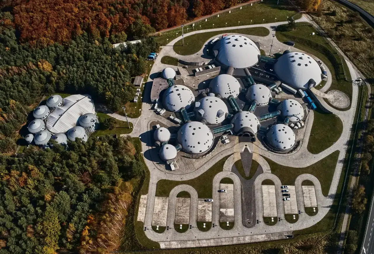 Architektoniczny kompleks przypominający alvernia planet, z kopułowymi budynkami otoczonymi lasem i parkingiem.