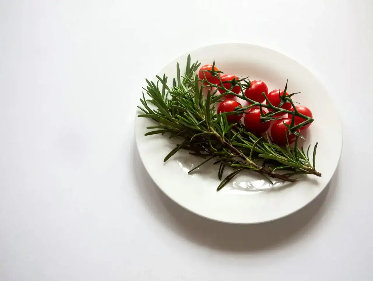 Gałązka rozmarynu z pomidorkami koktajlowymi na białym talerzu. Rozmaryn do czego? Do aromatycznych potraw!