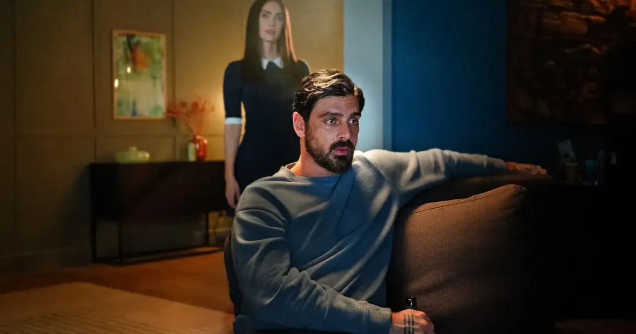 Michele Morrone w filmach, siedzi na kanapie, a za nim stoi kobieta.
