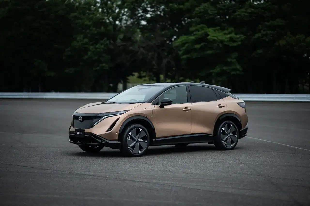 Elegancki, brązowy Nissan Ariya na tle zielonych drzew i asfaltu.