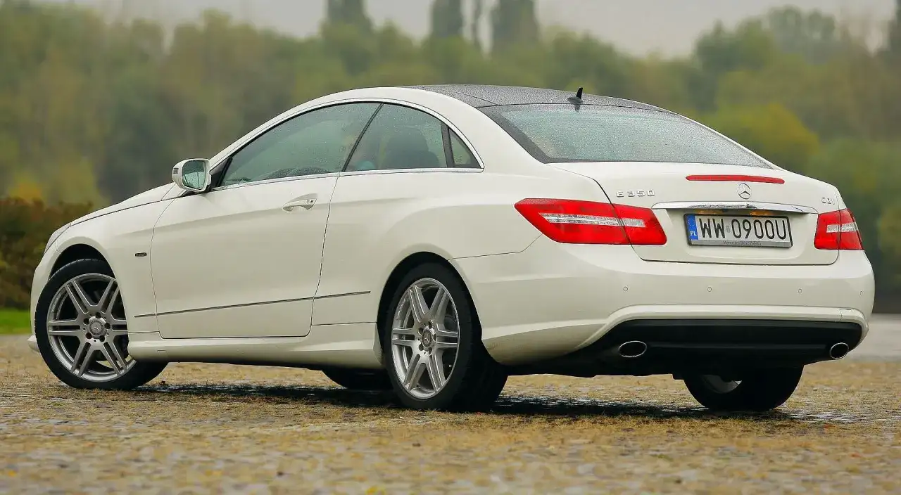 Biały w212 coupe z polskimi tablicami rejestracyjnymi stoi na mokrej nawierzchni.