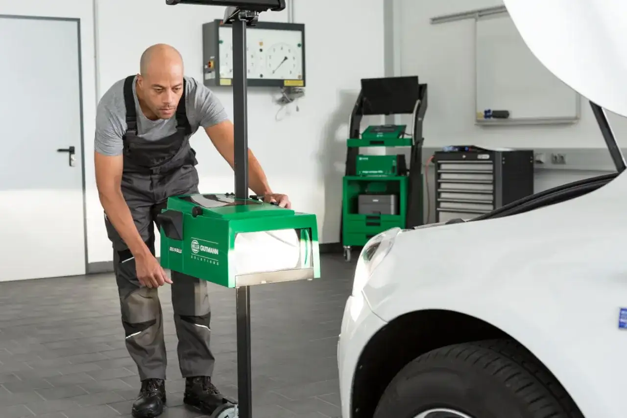 Un mécanicien ajuste un appareil de mesure pour vérifier l'alignement des phares d'une voiture. Cet outil est essentiel pour savoir a quoi sert un phare : éclairer la route en toute sécurité.