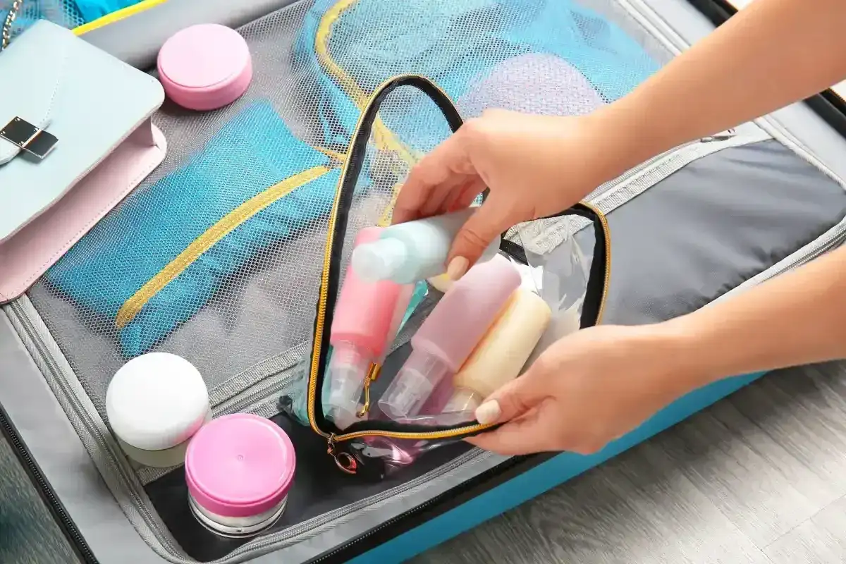Ręka wkłada do bagażu podręcznego Ryanair małe, kolorowe buteleczki z kosmetykami, w tym szklane perfumy.
