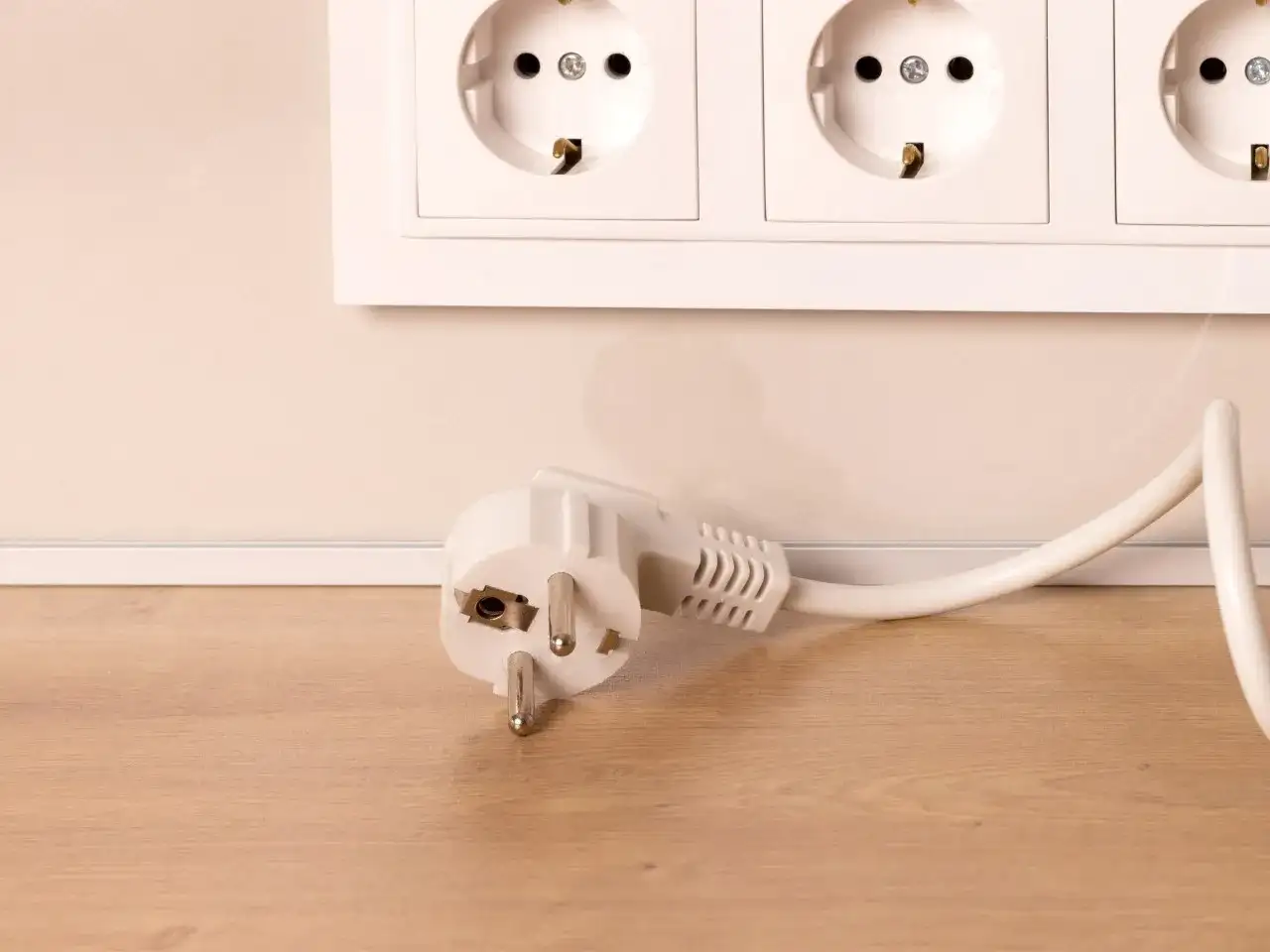 Biały eurozłącze leży na drewnianej podłodze, obok gniazdek elektrycznych.
