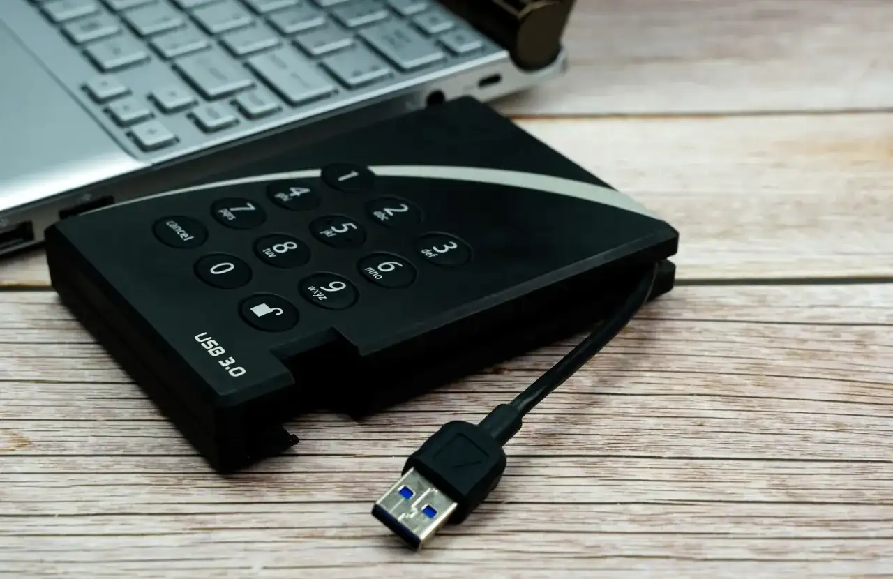 Dysk zewnętrzny z klawiaturą numeryczną i kablem USB 3.0 obok laptopa, gotowy do udostępniania internetu z telefonu na komputer przez USB.