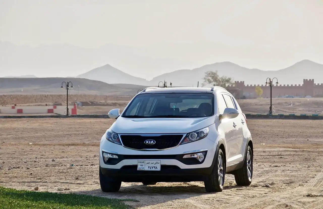 Białe Kia Sportage, jeden z popularnych modele kia, zaparkowany na pustynnym terenie z górami w tle.