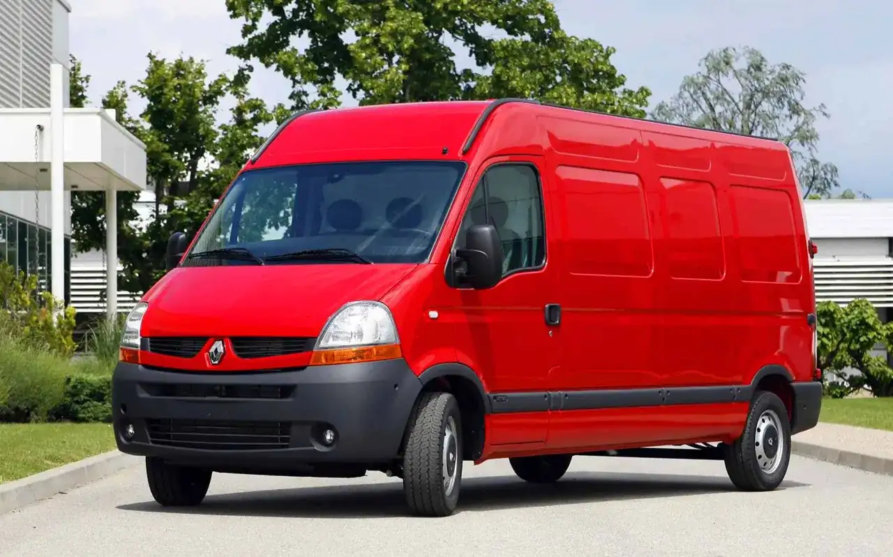 Czerwony Renault Master 2, gotowy do pracy, stoi na tle zieleni i nowoczesnego budynku.