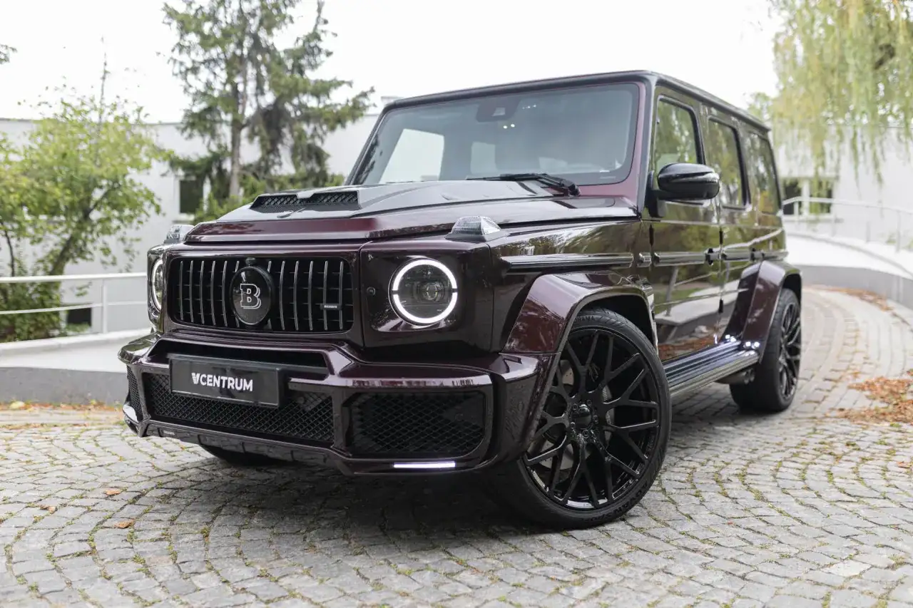 Mocarny Brabus 700 w bordowym kolorze, z czarnymi felgami i charakterystycznym grillem, prezentuje się imponująco na brukowanej nawierzchni.
