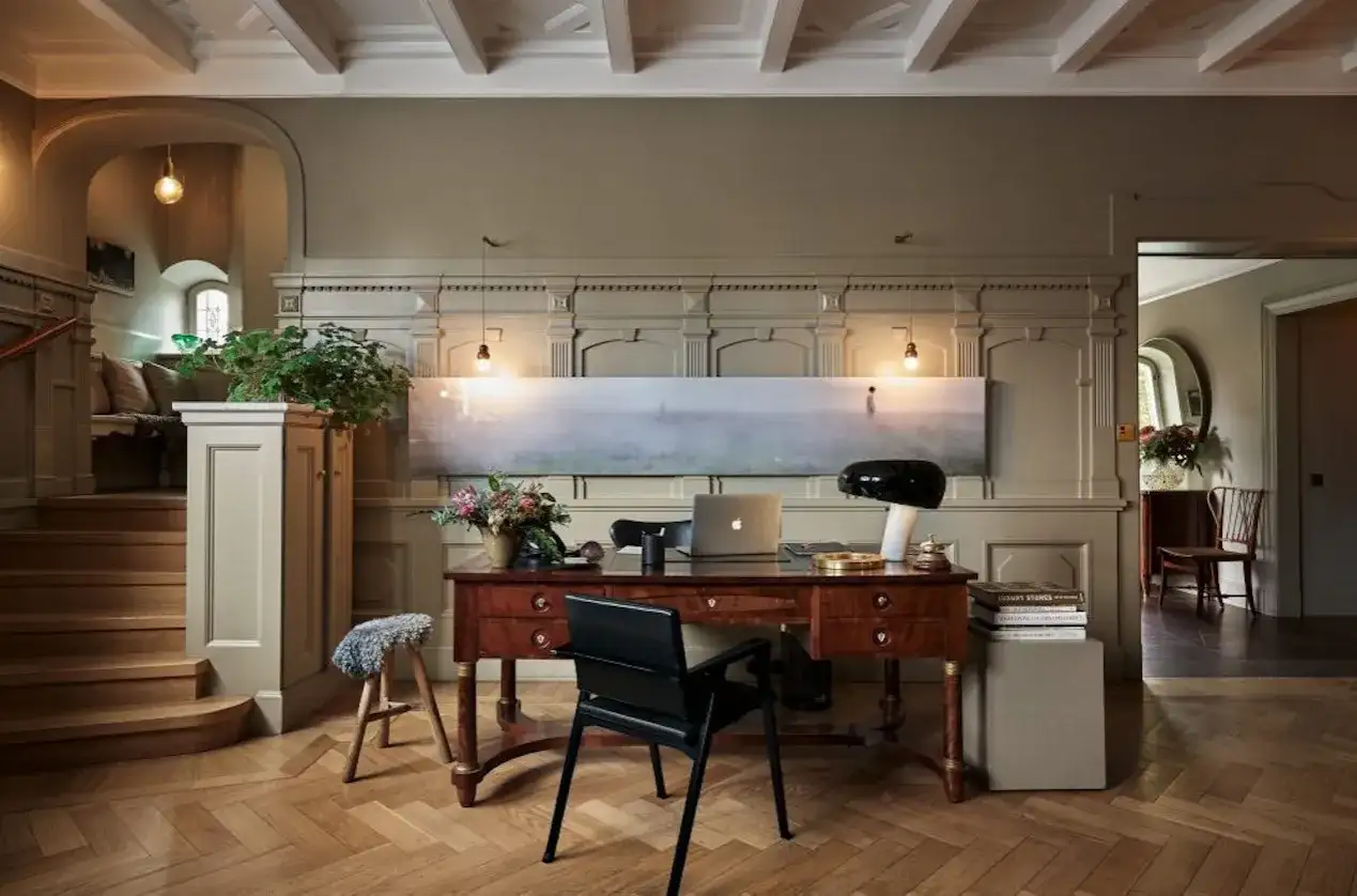 Ett elegant skrivbord med laptop och lampa, i en hall med trappa och konst. Martin Brudnizki-inspirerad design.