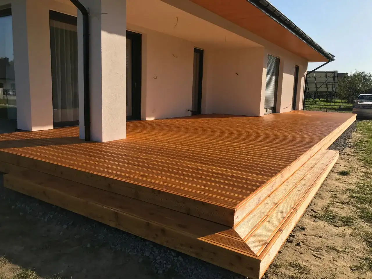Nowa, drewniana terasa z widocznymi stopniami, zabezpieczona impregnatem do legarów tarasowych, lśni w słońcu.