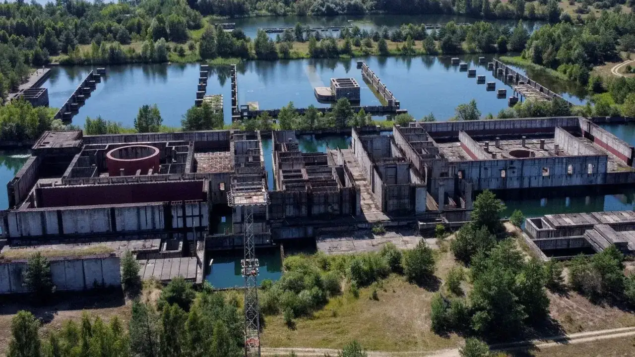 Niedokończona elektrownia w Żarnowcu, z betonowymi konstrukcjami i basenami wypełnionymi wodą, otoczona zielenią.