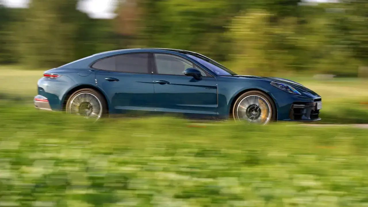 Niebieski Porsche Panamera Turbo S pędzi przez zielone pole, rozmazując krajobraz.