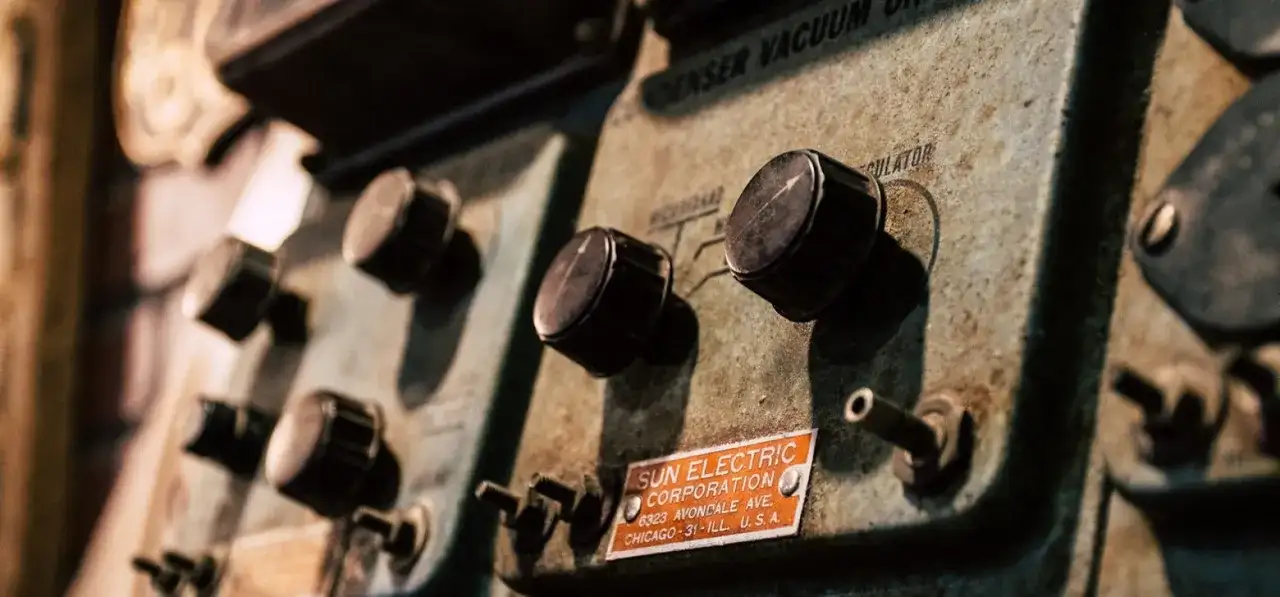 Stare pokrętła na panelu urządzenia Sun Electric Corporation. Widać napis "CONDENSER VACUUM REGULATOR" i adres firmy. To może być część starego warystora.