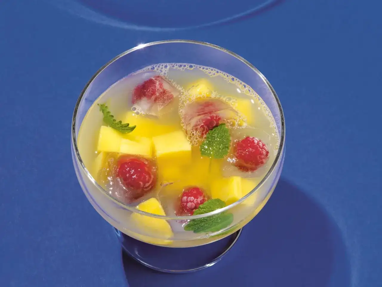 Erfrischende alkoholfreie Bowle mit Mango, Himbeeren und Minze in Eiswürfeln.