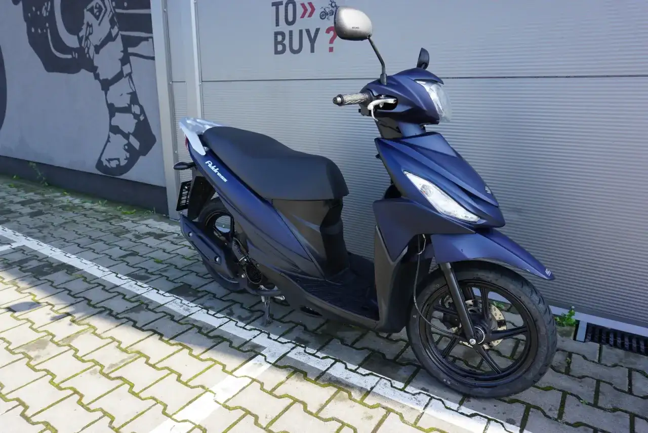 Elegancki, granatowy skuter Suzuki Address 110 zaparkowany na kostce brukowej.