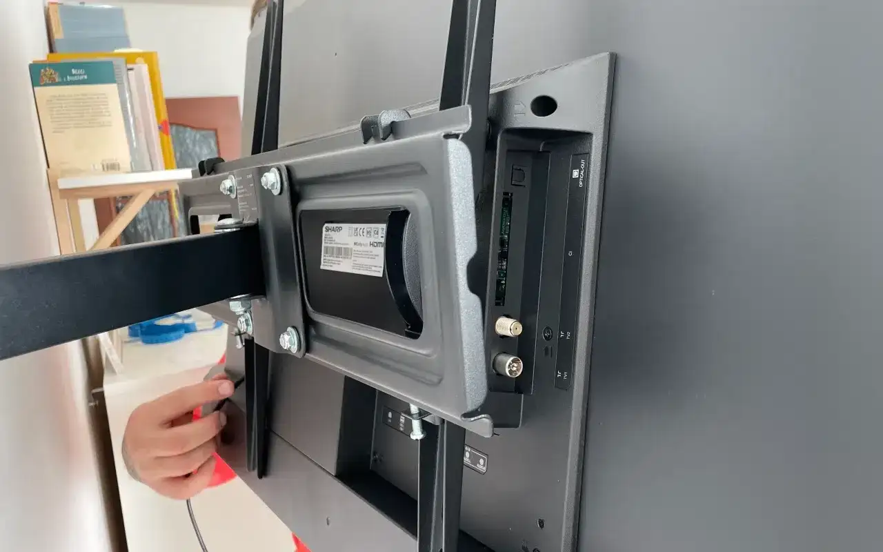 Montaż uchwytu do telewizora na ścianie z regipsu. Widoczne śruby i złącza.