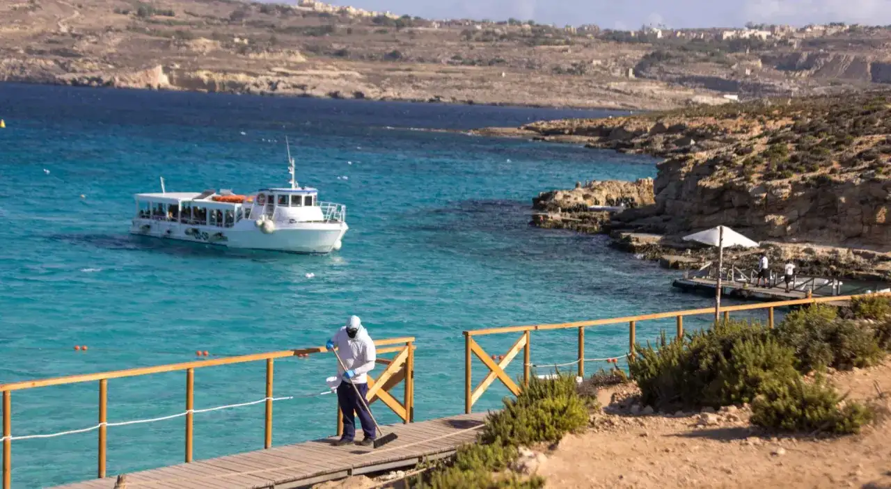 Malta, lipiec: słoneczna pogoda zachęca do rejsu statkiem po turkusowej wodzie. Pracownik sprząta drewniany pomost.
