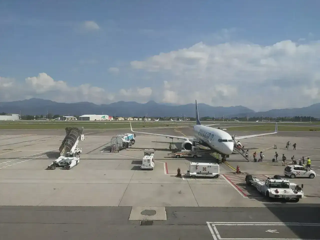 Samolot Ryanair na płycie lotniska Bergamo. W tle góry i budynki lotniskowe.