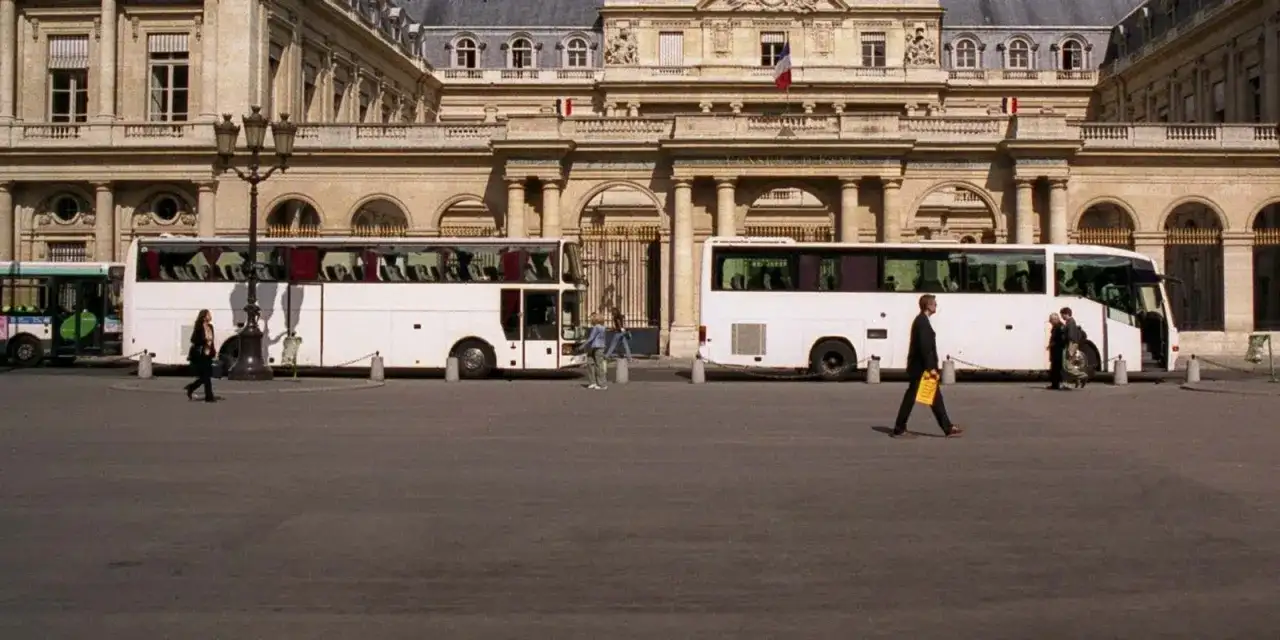 Weiße Reisebusse vor einem prächtigen Gebäude. Eine Frau geht vorbei. Wie kommt man am besten nach Paris? Mit dem Bus!