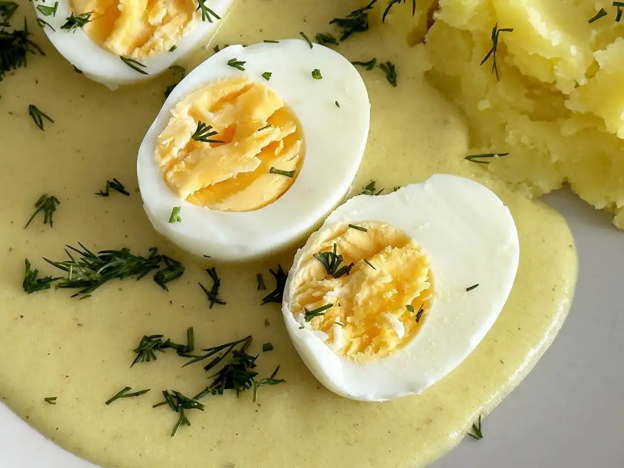 Jajka w sosie musztardowym, udekorowane koperkiem, obok purée ziemniaczane. Pyszne danie na obiad.