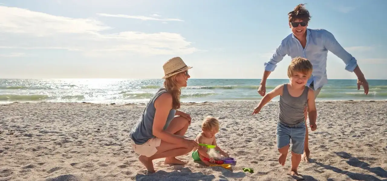 Rodzina cieszy się wakacjami gdzie nad morze z dzieckiem. Mama z tatą obserwują bawiące się maluchy na piaszczystej plaży.
