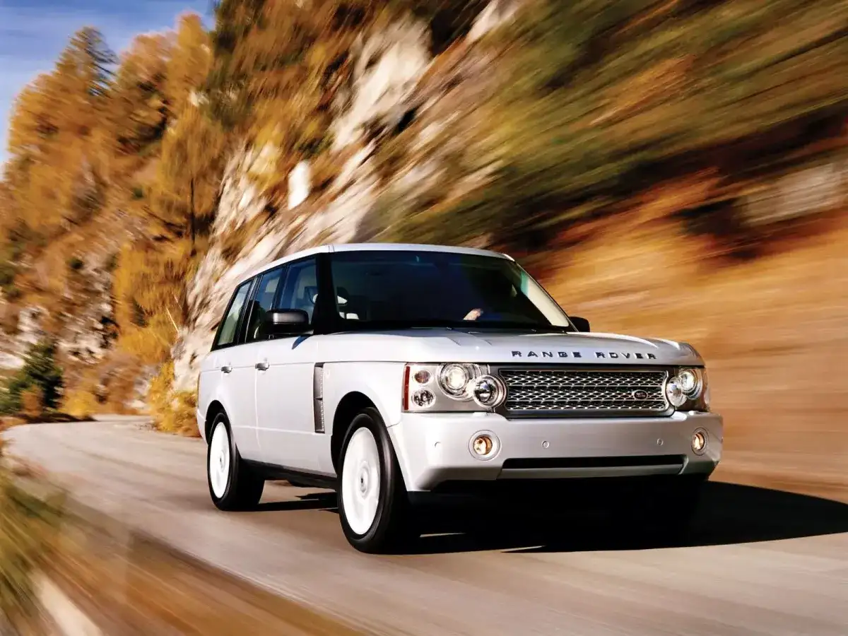 Biały Range Rover L322 pędzi po krętej drodze wśród jesiennych drzew.