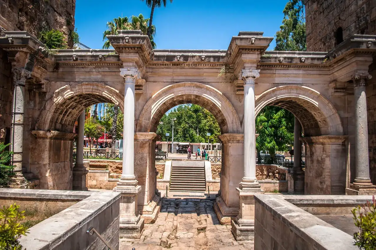 Łuk Hadriana, brama do **Antalya stare miasto**. Kamienne łuki i kolumny, w tle schody i zielone drzewa.