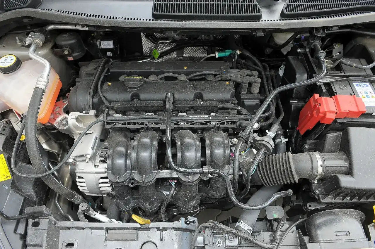 Silnik Ford Fiesta 2011 z widocznym kolektorem dolotowym, alternatorem i akumulatorem.