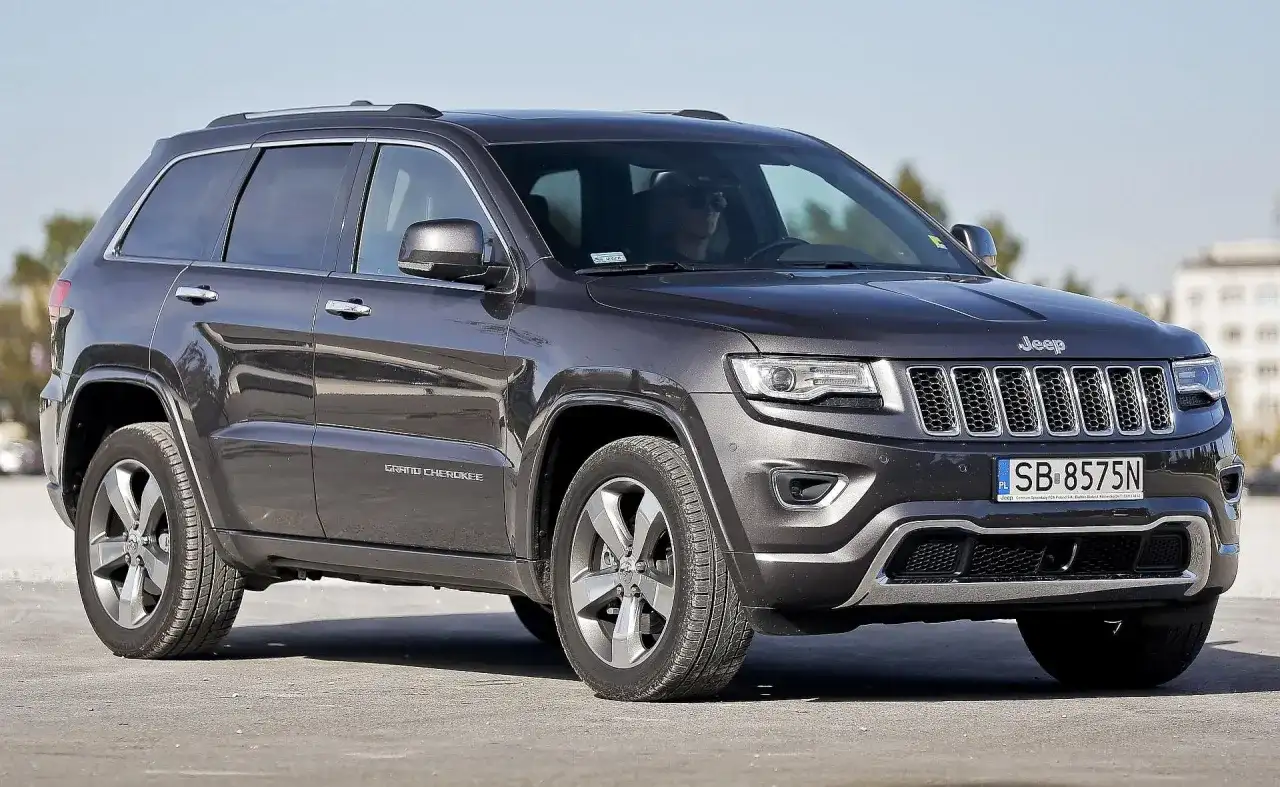 Ciemnoszary Jeep Grand Cherokee WK2 z polskimi tablicami SB 8575N zaparkowany na zewnątrz.