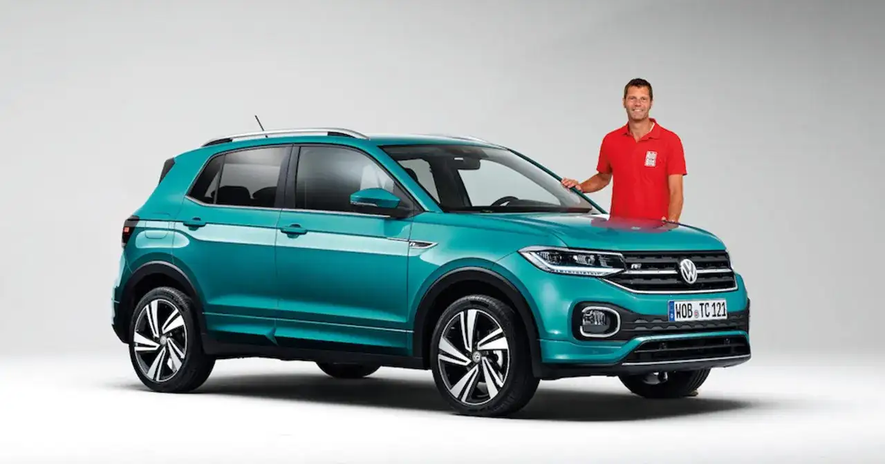 Mężczyzna w czerwonej koszulce stoi obok turkusowego Volkswagena T-Cross, który przekracza wymiary miejskiego auta.