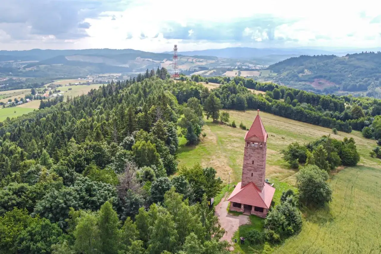 Kamienna wieża widokowa na wzgórzu, otoczona lasem i polami, oferuje wspaniałe widoki na krajobraz Dolnego Śląska.