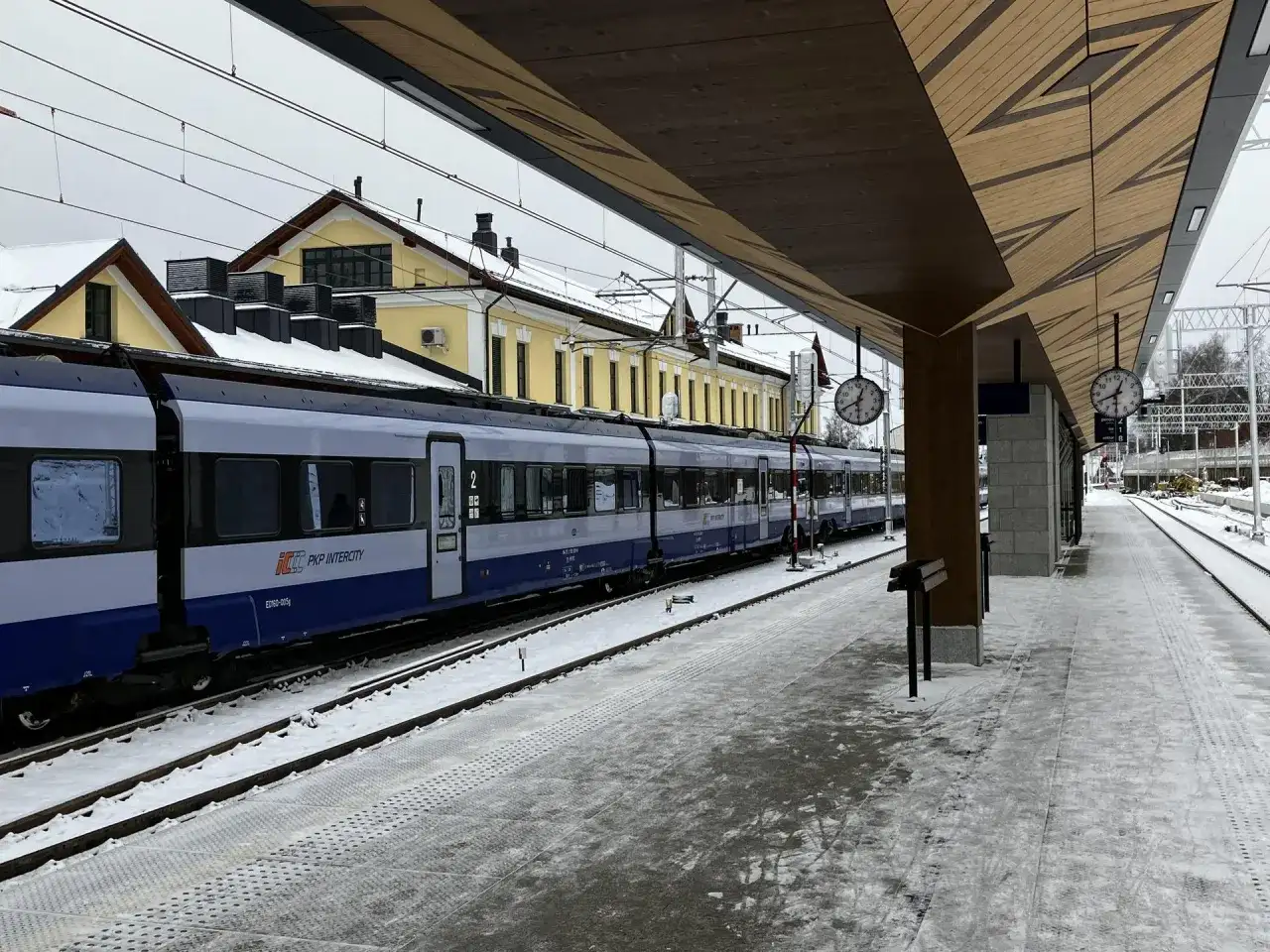 Pociąg PKP Intercity na stacji w Żaganiu, zimowy dzień. Zielona góra w oddali, śnieg na torach i peronie.